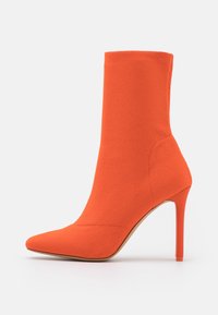 Botte de cheville orange en tissu texturé avec un bout pointu et un talon aiguille, présentant un design sans couture et une finition lisse.