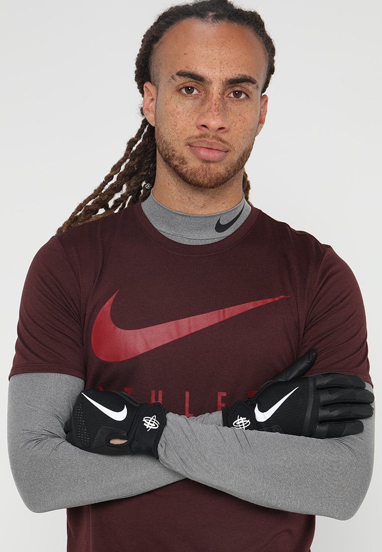 Svarte treningshanske med teksturert overflate, med en hvit logo. Brukt av en person i en burgunder Nike skjorte og grå langermet genser.