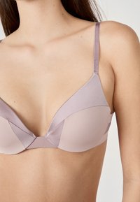 Soutien-gorge violet clair avec une finition satinée lisse, doté d'un décolleté en V et de bretelles réglables, mettant en valeur un bloc de couleurs géométrique.
