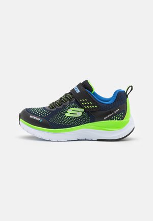 Zapatilla deportiva negra y azul con una parte superior de malla transpirable, acentos en verde lima, una suela blanca acolchada y correa ajustable. Etiquetada como impermeable.