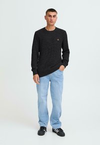 Pulover negru din tricot cu textură în relief și guler rotund, asortat cu blugi bleu deschis și adidași negri cu accente albe.