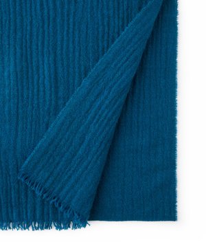 Blødt blå strikket stof med ribbet struktur, delvist foldet for at vise lag og frynser på kanterne.