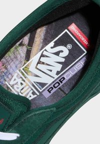 Plantilla de zapatilla Vans verde con tela texturizada, que presenta un estampado gráfico y un logotipo. Los acentos incluyen un borde acolchado y una marca etiquetada.