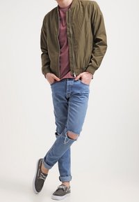 Olivová bombardérka, vínové tričko, světle modré roztrhané džíny a šedé slip-on boty s bílou podrážkou. Jednoduchý, neformální outfit.