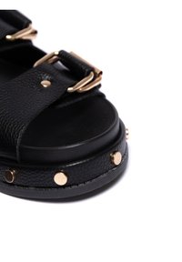 Černé kožené sandály s texturovanými pásky, zlatým kováním, plochou podrážkou a dekorativními zlatými hřebíky podél spodní části.