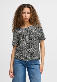 Blusa a fantasia in bianco e nero con vestibilità ampia, scollatura rotonda e maniche corte, abbinata a jeans in denim blu chiaro.