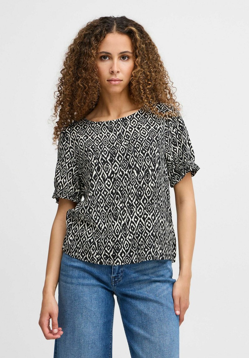 Blusa a fantasia in bianco e nero con vestibilità ampia, scollatura rotonda e maniche corte, abbinata a jeans in denim blu chiaro.