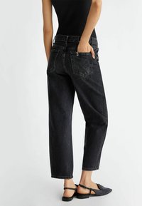 Vaqueros de mezclilla negros con un corte relajado, que cuentan con cinco bolsillos, una cremallera y dobladillos deshilachados. Combinados con zapatos negros de tiras.