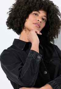 Zwarte denimjas met een kraag, lange, uitlopende mouwen, twee borstzakken en zilveren hardware-details. Glad textuur en een figuurvriendelijk ontwerp.