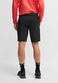 Pantaloni corti neri su misura con una texture liscia, lunghezza fino a metà coscia e due tasche posteriori, abbinati a una maglietta a maniche lunghe color corallo e calzini neri.