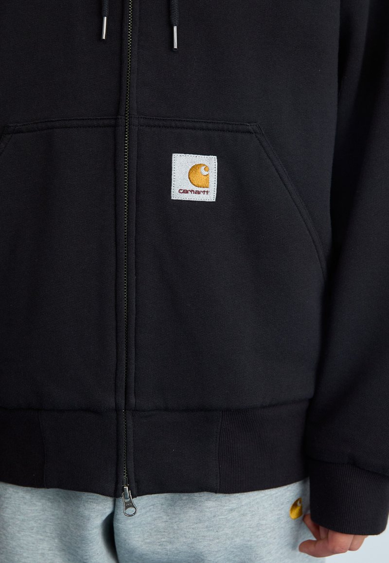 Schwarze Fleece-Zip-Hoodie mit gerippten Bündchen und Saum. Mit gesticktem Carhartt-Logo auf einem quadratischen Patch.