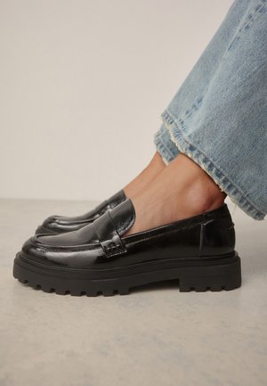 Black patent leather loafers with a chunky rubber sole and rounded toe, featuring a stitched vamp and smooth surface texture.