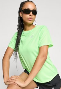 Ελαφρύ αθλητικό πουκάμισο κοντομάνικο σε χρώμα λαχανί με λεία υφή και μικρό λογότυπο στο στήθος. Μαύρα γυαλιά ηλίου ολοκληρώνουν την εμφάνιση.