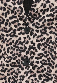 Veste à imprimé léopard avec deux grands boutons noirs et un col sur un haut noir texturé.