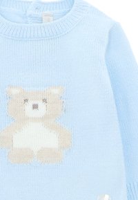 Suéter de punto azul claro con un diseño de oso en crema y marrón en la parte delantera, con un cuello acanalado y detalles de botones en el hombro.