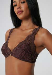 Mauve Spitzen-Bralette mit floralem Muster, dünnen verstellbaren Trägern und einem dekorativen Mittelpunkt, der ein kompliziertes, strukturiertes Design aufweist.