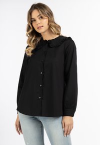Schwarze Button-Down-Bluse mit Rüschensaum und langen Ärmeln. Aus glattem Stoff mit lässiger Passform und subtiler Schattierung.