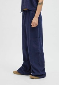 Marineblauwe brede broek gemaakt van een lichtgewicht stof, met een elastische tailleband, trekkoord en een zijzak.