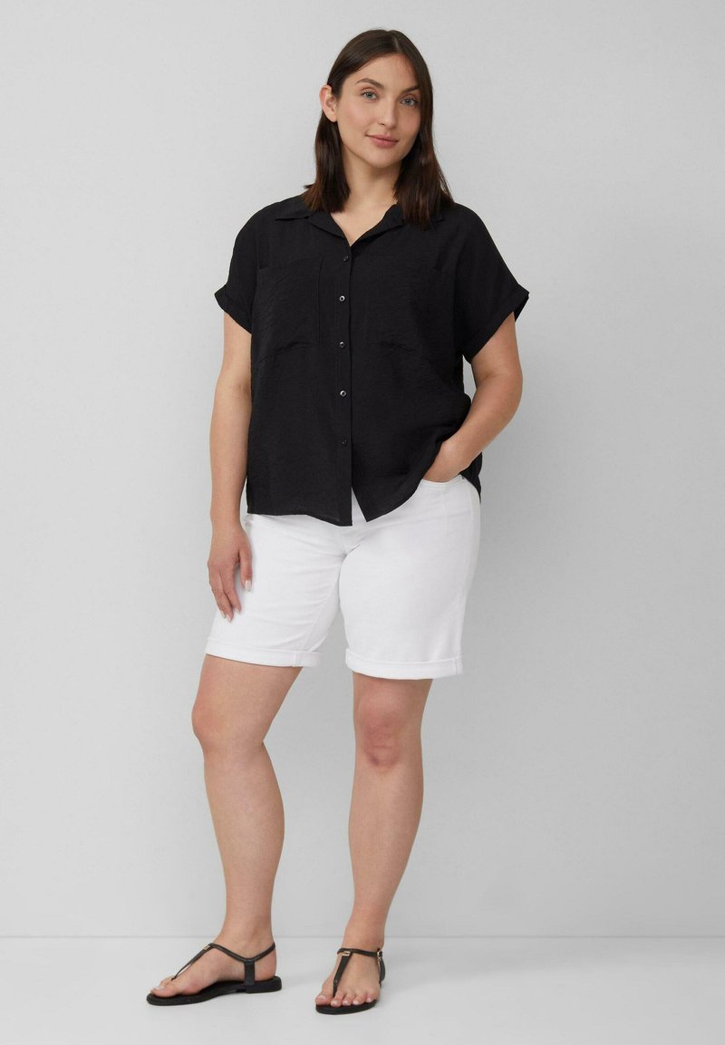 Zwarte korte mouwen overhemd met knopen en twee borstzakken, gecombineerd met witte shorts met opgerolde manchetten en platte zwarte sandalen.