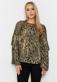 Langärmlige Bluse im Schlangendruck mit einer beige und schwarzen Farbkombination. Verfügt über fließende Ärmel und einen leichten Stoff.