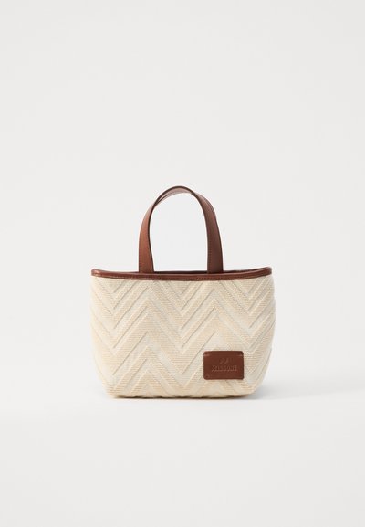 Sac fourre-tout tissé avec un motif en chevrons crème, poignées en cuir marron et une étiquette marron sur le devant. Design compact et structuré.