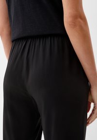 Pantalon noir à taille élastique en tissu lisse et fluide. Gros plan sur l'arrière présentant une taille froncée et un design épuré et minimaliste.
