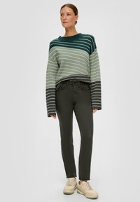 Pull en maille avec des rayures horizontales vertes, associé à un pantalon ajusté vert foncé et des baskets beiges. Le pull présente des manches larges et des poignets côtelés.