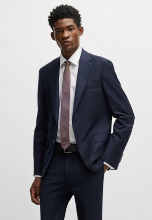 Mørkeblå skræddersyet jakkesæt med en hvid skjorte og mønstret slips. Jakkesættet har en slim fit og klassiske klapper, med diskrete lommer og en poleret finish.