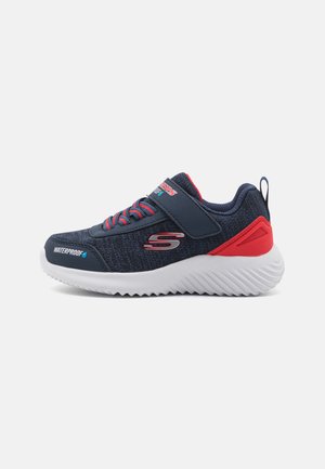 Baskets imperméables bleu marine avec des accents rouges, présentant une tige texturée, une sangle ajustable et une semelle en caoutchouc blanc avec un motif en zigzag.