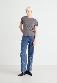 Grå bomull T-skjorte kombinert med blå denimjeans med stjernebroderi. Ribbete halslinning, avslappet passform og ankellengde. Svarte ankelstøvler.