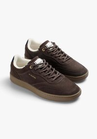 Bruna mockaskor med gummisula, rund tå och perforerad design. Har guldfärgade öglor och varumärkeslogotyp på tungan.