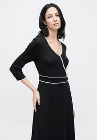 Fekete ruha háromnegyedes ujjakkal, mély V-nyakkivágással és fehér szegéllyel. Puha anyag, testhez simuló derékrész és lenge szoknya.