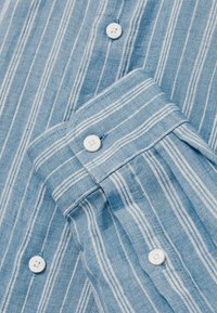 Tissu bleu clair avec des rayures verticales blanches, avec des boutons blancs sur le poignet de la chemise et la patte de boutonnage avant.