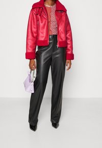 Veste courte en cuir rouge avec col en fausse fourrure, associée à un pantalon large en cuir noir et un petit sac à main lavande.