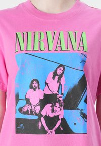 Rosa bomulls T-skjorte med grafisk trykk av fire figurer mot en blå bakgrunn, med "NIRVANA" tekst i livlig grønn.