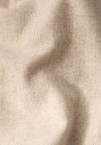 Beige stof med en blød, tekstureret overflade. Lidt krøllet med et subtilt mønster, der fremviser forskellige nuancer af creme og lys brun.