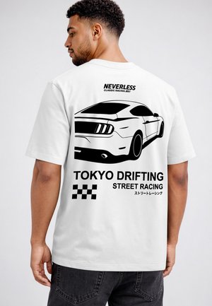 Man wearing a white t-shirt with a black graphic of a sports car and text "Neverless Classic Racing," "Tokyo Drifting Street Racing," and a checkered flag.