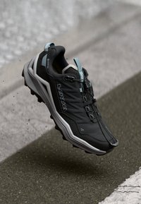 Black trail running shoe with a textured upper, white midsole, and light blue accents. Features a lace system and GORE-TEX branding.