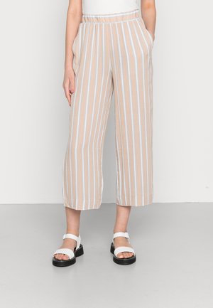 Woman wearing beige wide-leg cropped pants with white vertical stripes and white platform sandals, standing against a plain background.