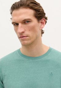 Light green cotton t-shirt featuring a crew neckline and a small skull logo on the chest. Smooth texture with a relaxed fit.