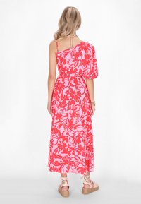 Rochie maxi cu un singur umăr, roz cu modele florale mari roșii, are o talie gathered și o fustă în straturi; asortată cu sandale cu toc mic, ușoare.