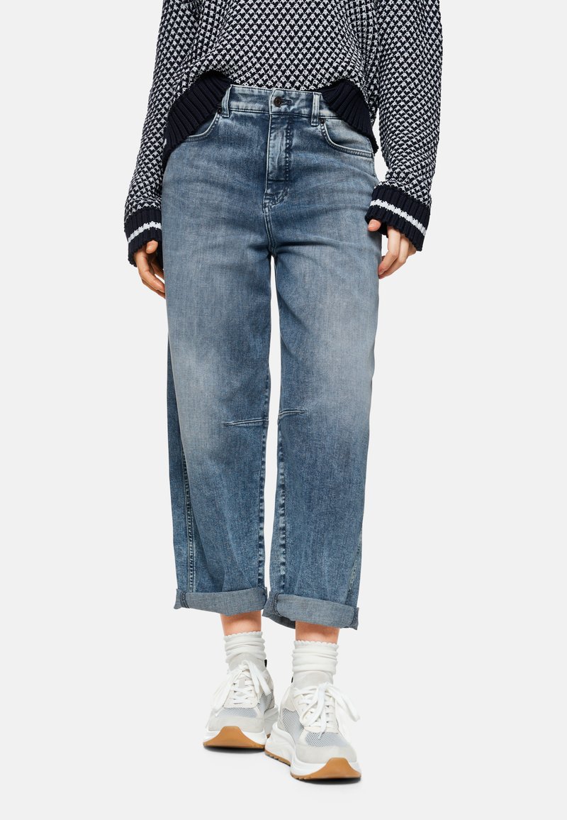 Light blue denim jeans with a relaxed fit, featuring rolled cuffs and subtle distressed detailing, paired with white sneakers and ribbed socks.