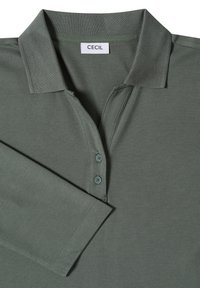 Polo vert à col avec trois boutons et manches longues pliées, étiqueté "CECIL" sur l’étiquette intérieure du col.