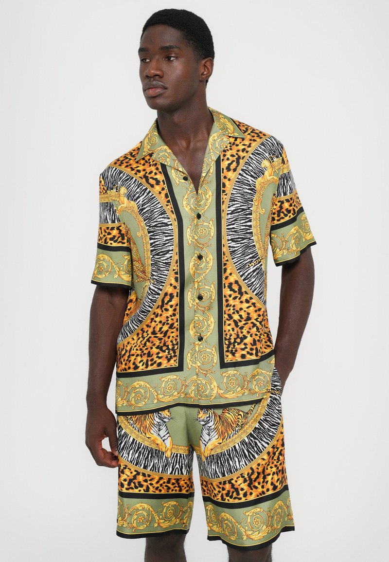 Korte mouwen knoopshirt en bijpassende shorts in groen, geel en zwart met dierenprints en gouden accenten, voorzien van ingewikkelde patronen.
