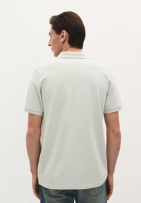 Polohemd in Hellgrau, aus strukturiertem Stoff. Mit Kragen und kurzen Ärmeln. Getragen mit dunkelblauen Jeans.