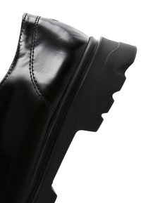 Stivaletto in pelle nera con finitura lucida, caratterizzato da cuciture a contrasto e una robusta suola in gomma nera spessa con un design del battistrada aggressivo.
