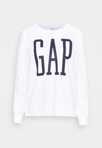 Bílá mikina s dlouhým rukávem a velkými námořnickými modrými písmeny "GAP" tištěnými na přední straně.