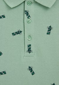 Ljusgrön polo skjorta med en texturerad tyg. Har flera broderade fyrar i grönt och marinblått, samt gröna knappar.