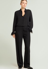 Zwarte zijden blouse met knoopsluiting en veeraccenten aan de manchetten, gecombineerd met zwarte, hooggetailleerde broek met een getailleerde pasvorm.