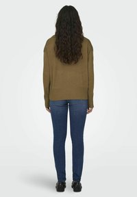 Pull olive avec ourlet côtelé, présentant une coupe décontractée et des épaules tombantes, associé à un jean foncé ajusté et des chaussures noires.